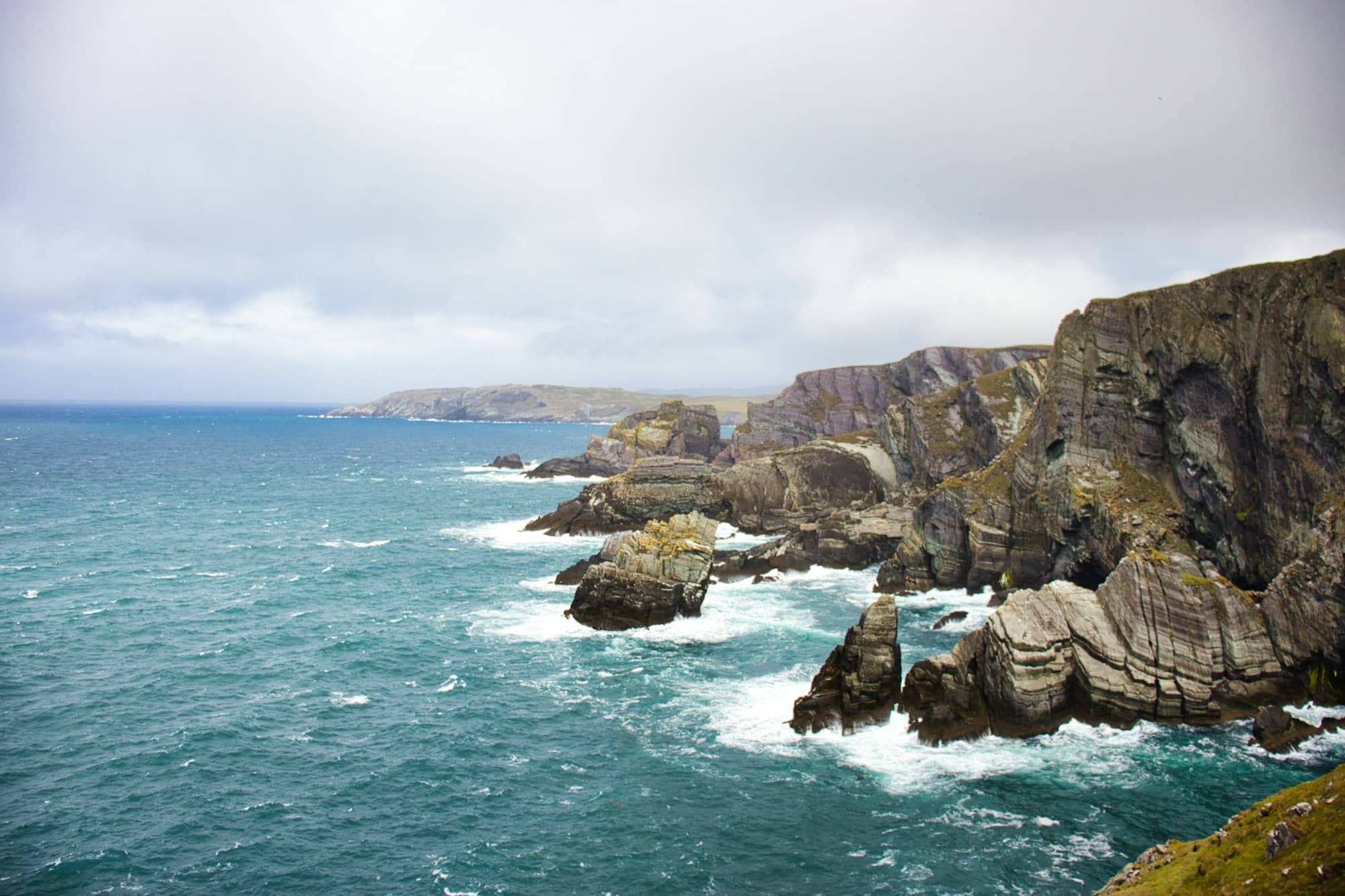 Rugged cliffs meet the ocean under a cloudy sky.