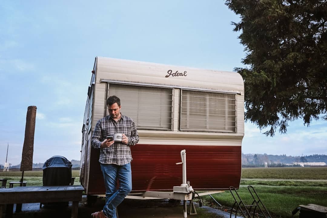 Man standing by vintage travel trailer holding a cup.