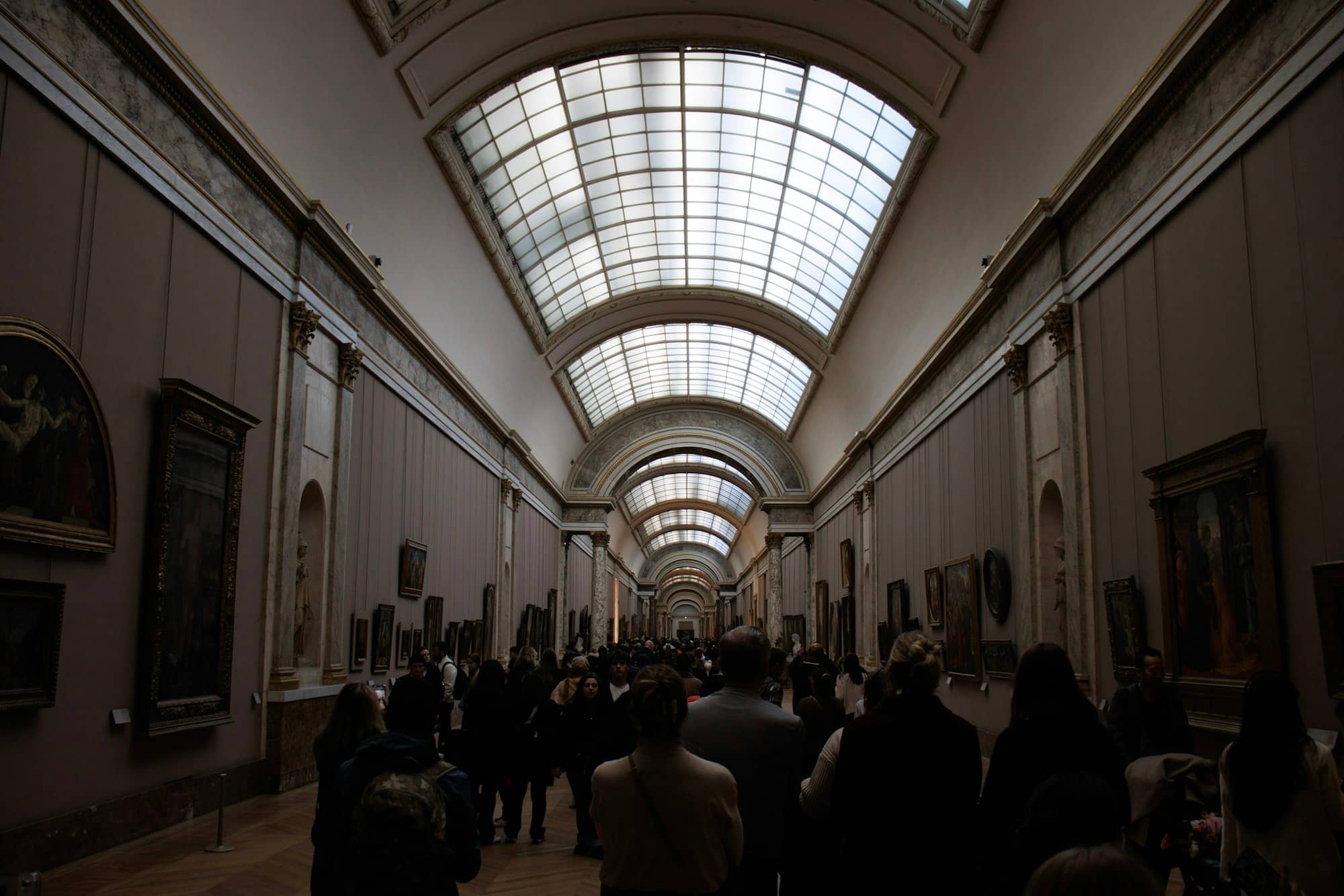 People walking through a long art gallery with paintings.