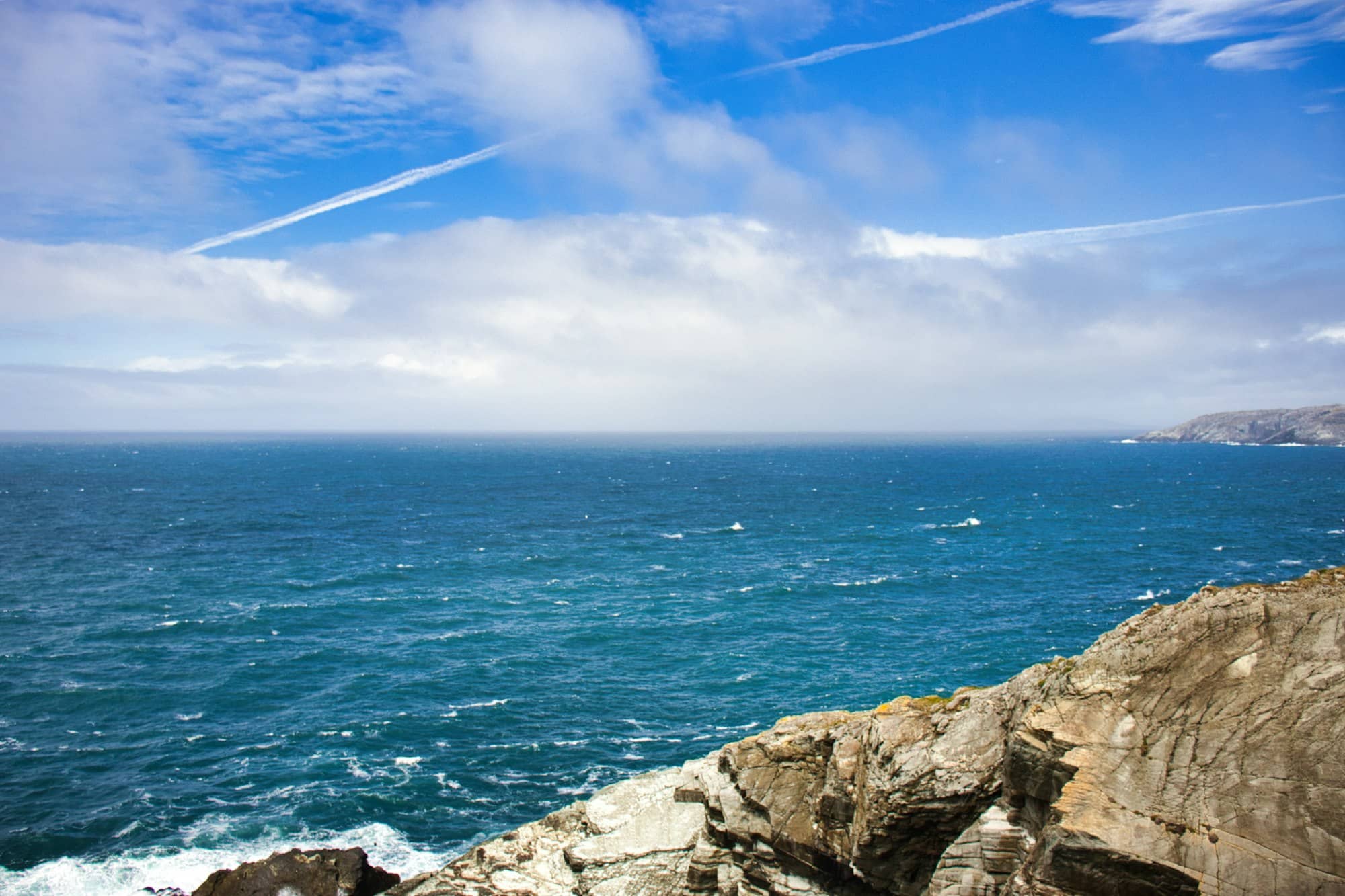 Ocean waves crash against rocky cliffs under a cloudy sky.