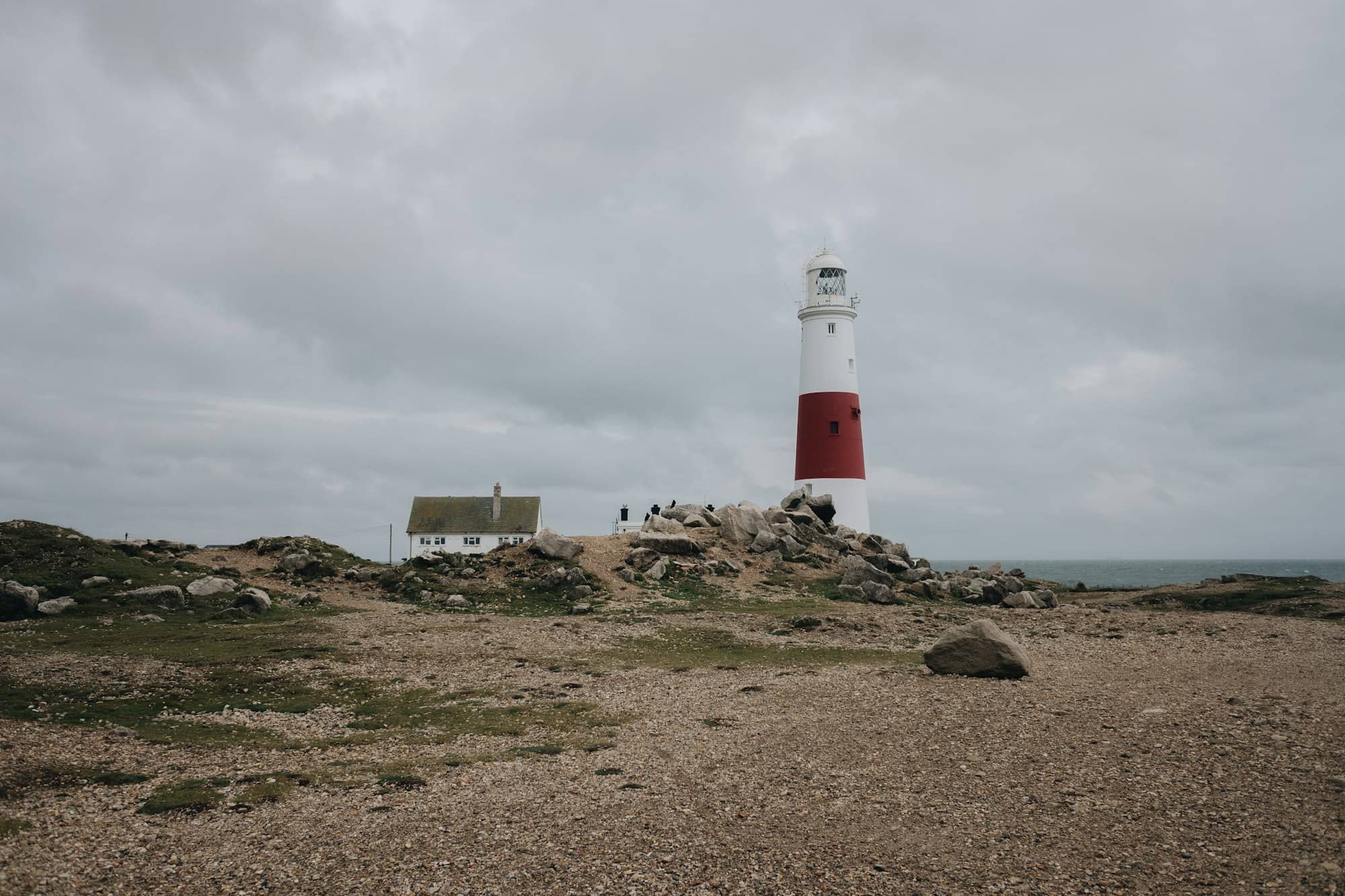 white and red lighthouse on brown sand near body of water during daytime