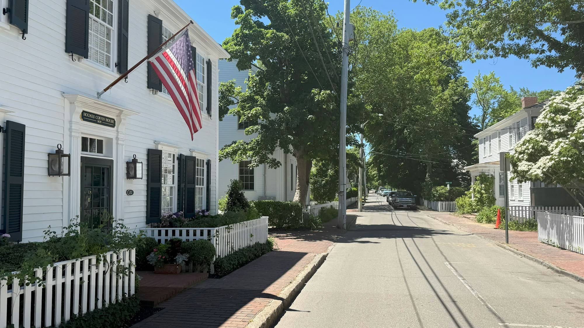 Traditional white house with american flag on a tree-lined street.