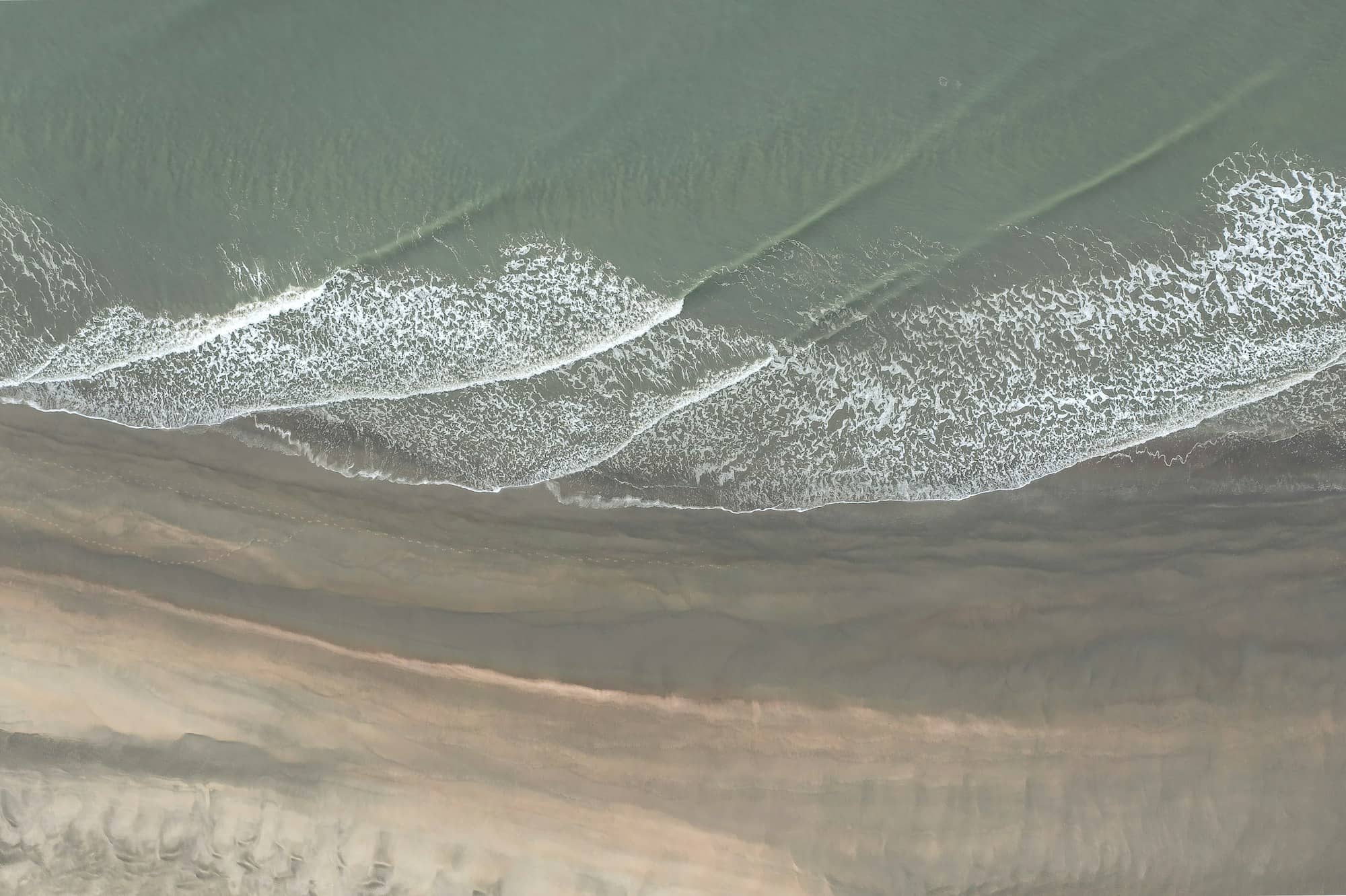 an aerial view of a sandy beach with waves
