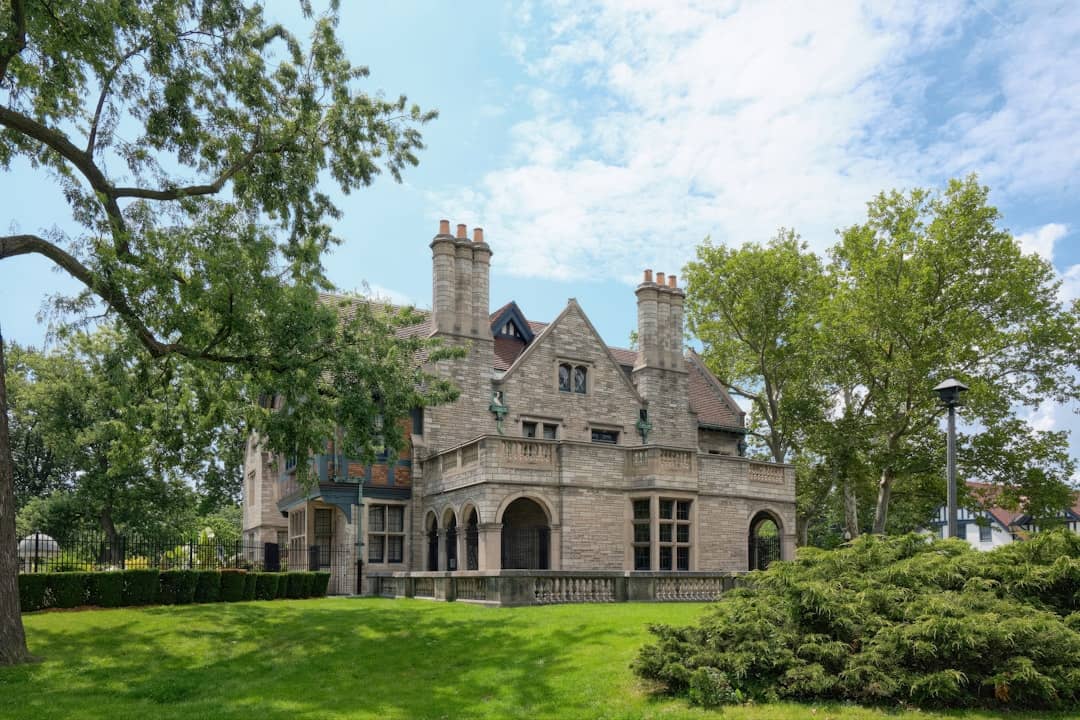 A large stone mansion with trees and green lawn.