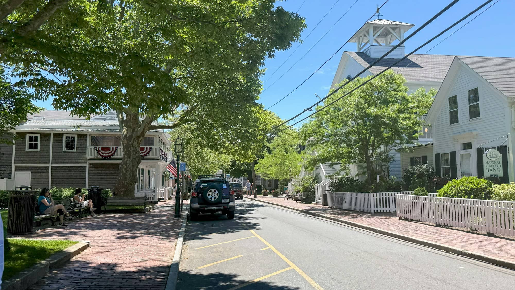 Quaint town street with houses, trees, and a church steeple.