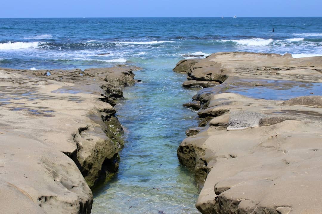 Clear water channel through rocky shore leading to ocean.