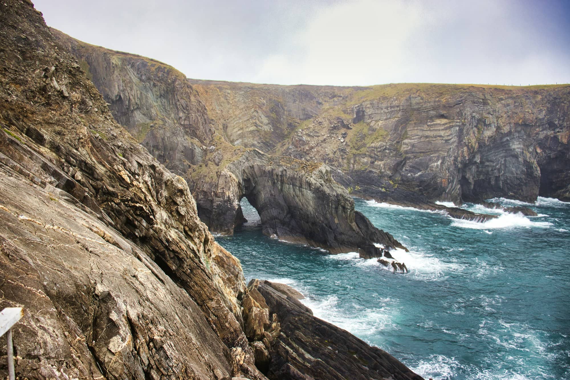 Rugged cliffs meet the turbulent blue ocean waves.