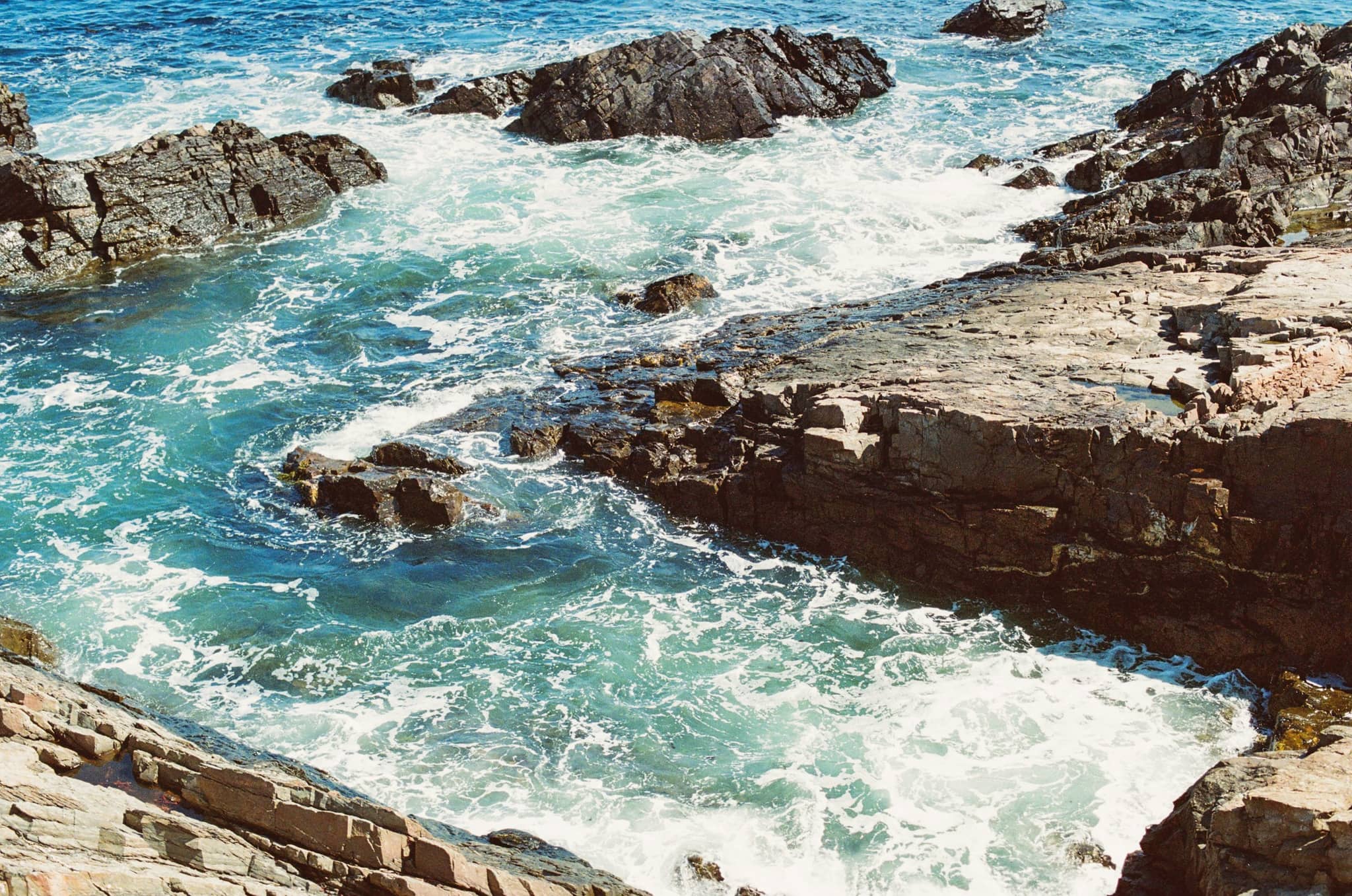 Turquoise water washing white over tilted rock ledges on an open stretch of Maine coast