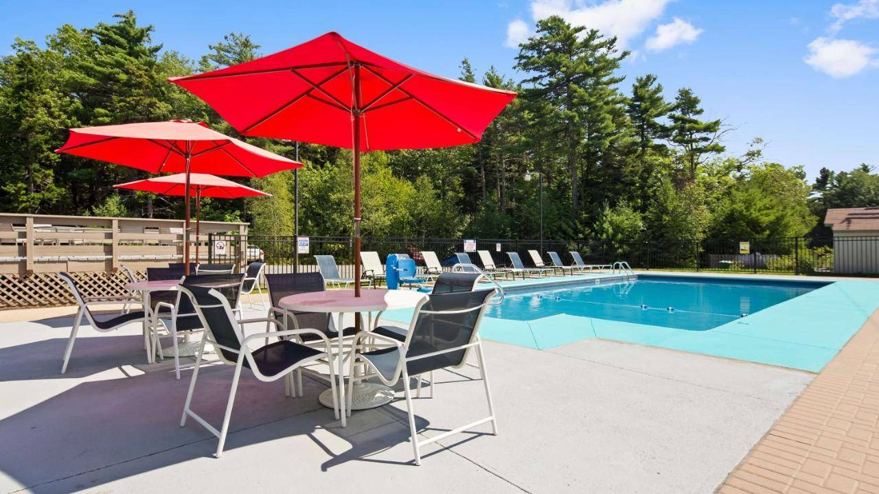 a patio with red umbrellas and chairs next to a pool at Best Western Acadia Park Inn in Bar Harbor