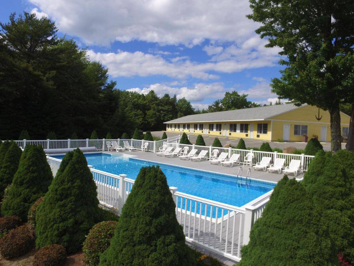 a swimming pool with chairs and trees and a building at High Seas Motel in Bar Harbor