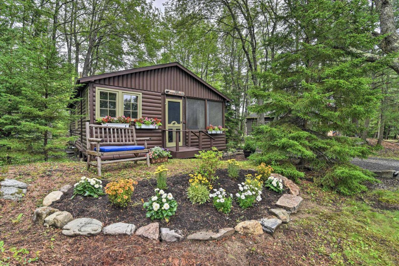 a small cabin in the woods with a bench and flowers at Sprucewold Boothbay Harbor Cottage with Deck in Boothbay Harbor