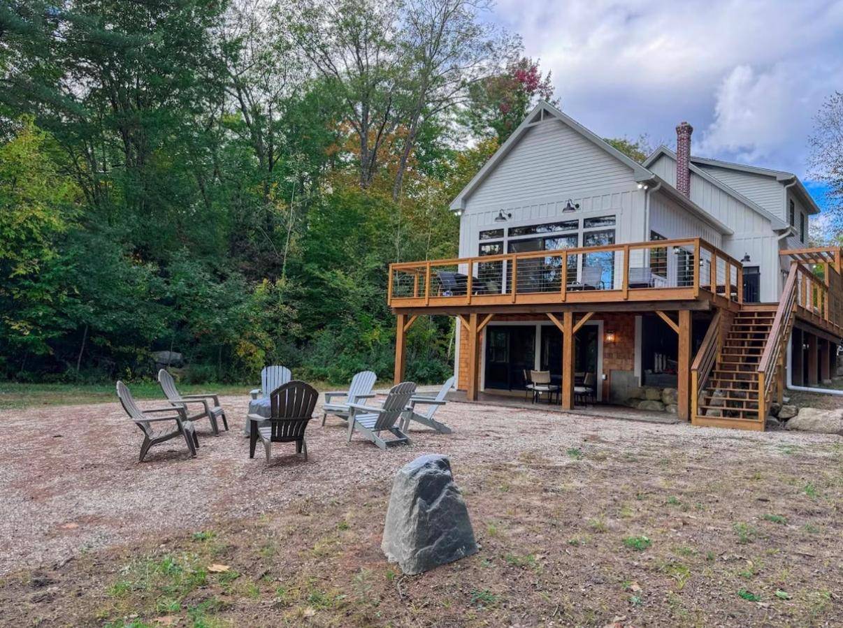 a large house with a deck and chairs in the yard at Long Lake - slice of heaven in Bridgton