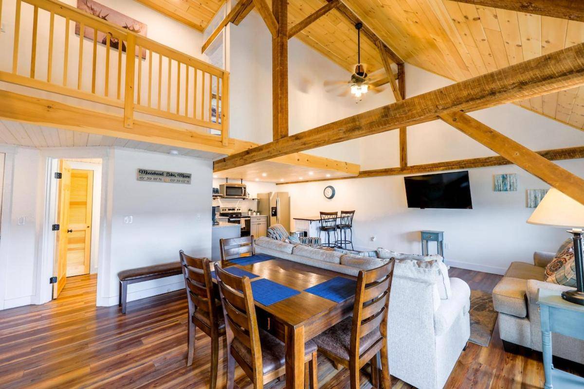 a dining room and living room with wooden ceilings at NEW! Historic post and beam in-town Moosehead Lake in Greenville