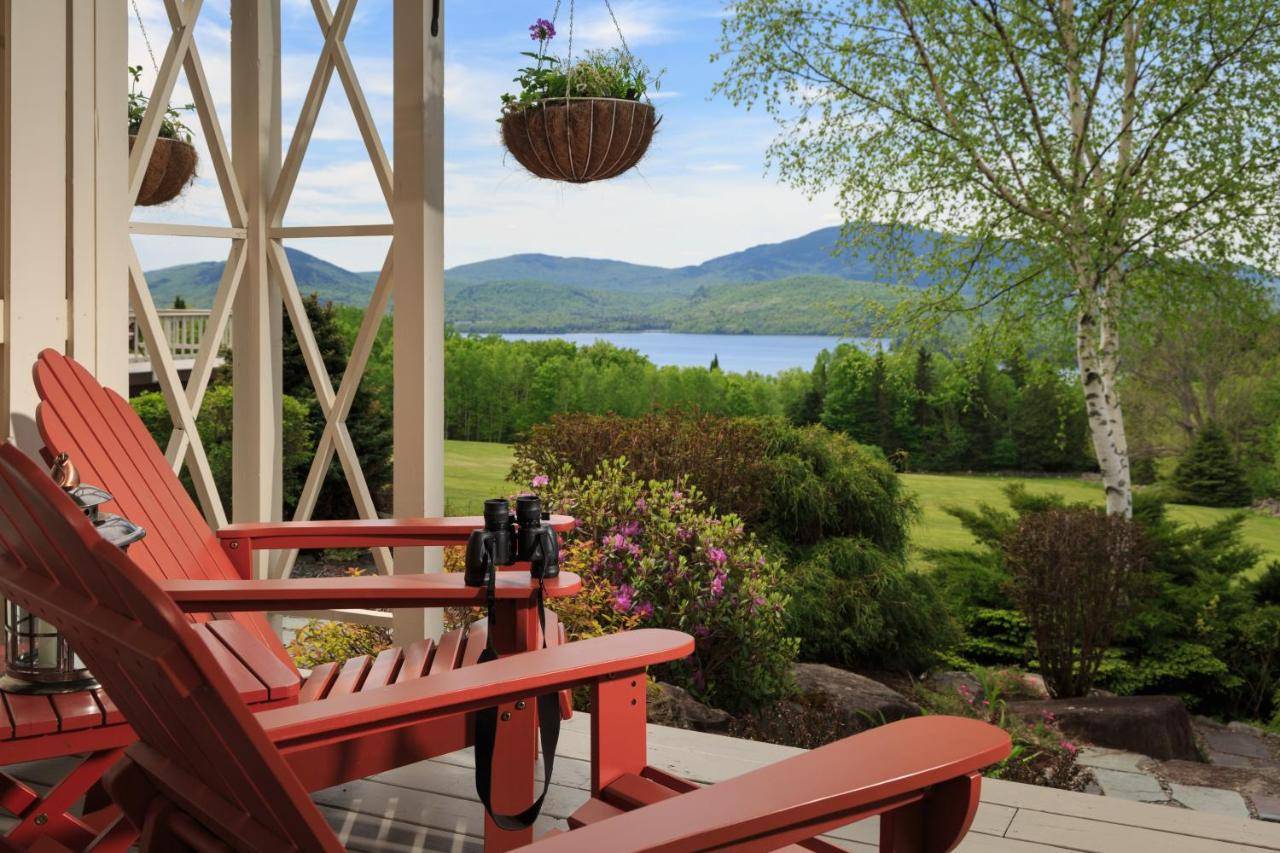 a pair of red chairs on a porch with a view of a lake at The Lodge at Moosehead Lake in Greenville