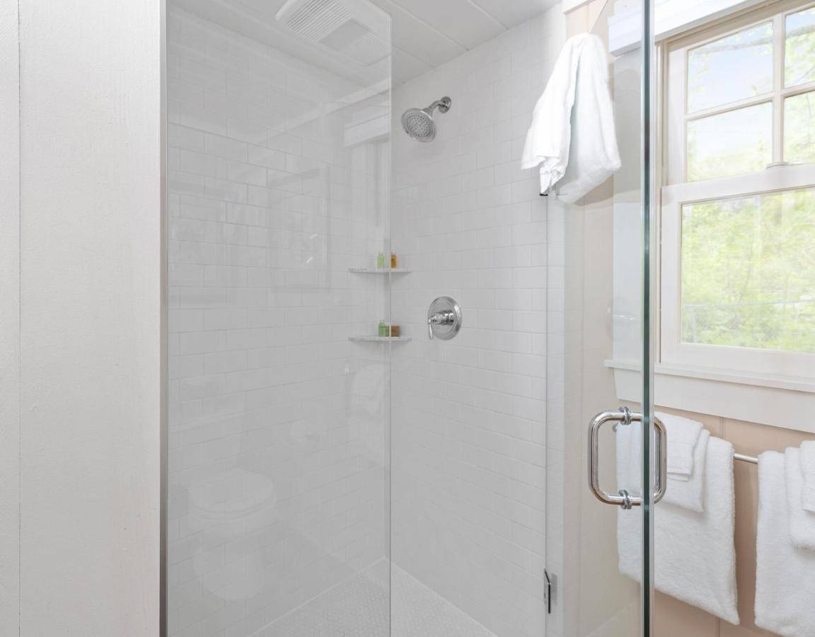 a white bathroom with a shower with a glass door at The Cottages at Cabot Cove in Kennebunkport