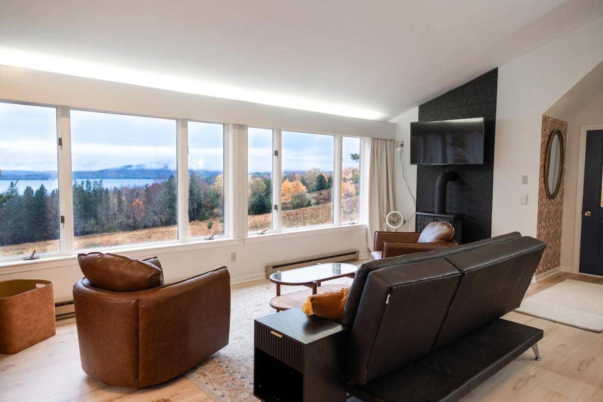 a living room with a couch and chairs and large windows at Airy Studio, Lake Access & Views, AC, 5min to Downtown in Rangeley
